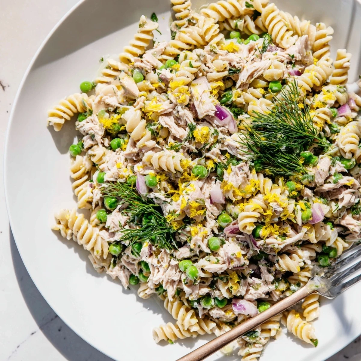 A vibrant bowl of Lemony Tuna Pasta Salad with flaked tuna, bright green peas, and fresh herbs tossed in a zesty lemon dressing.