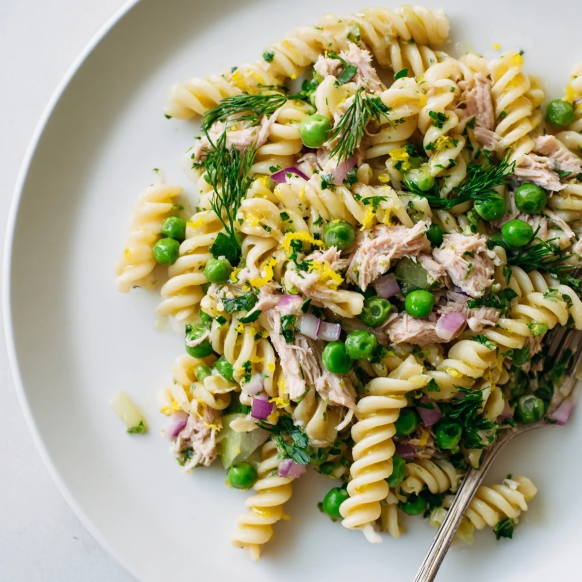 Picnic-ready Lemony Tuna Pasta Salad in a white serving bowl, garnished with dill and parsley, paired with a chilled glass of white wine.