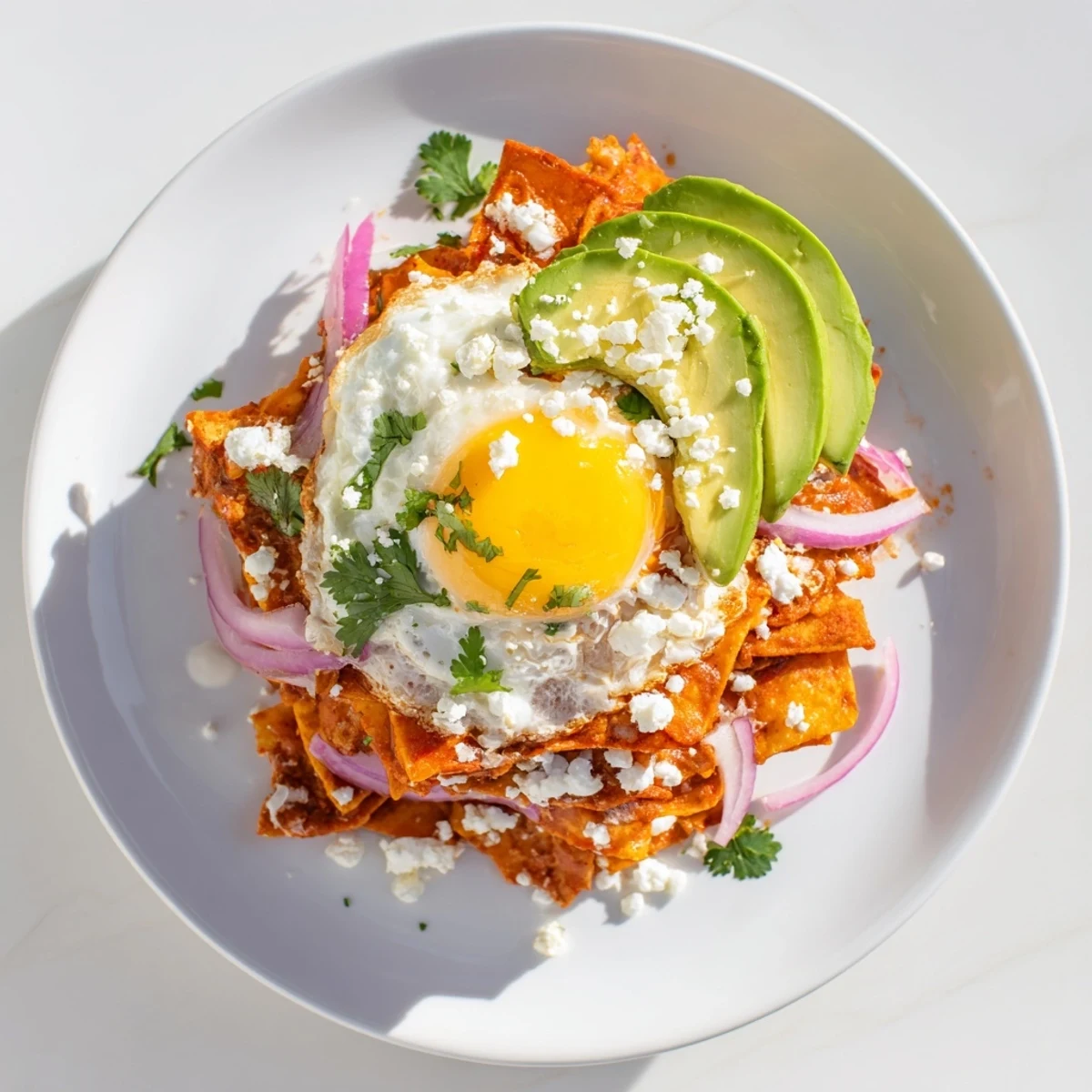 A hearty plate of homemade chilaquiles with fried egg, avocado slices, and crumbled cheese, perfect for a morning feast.
