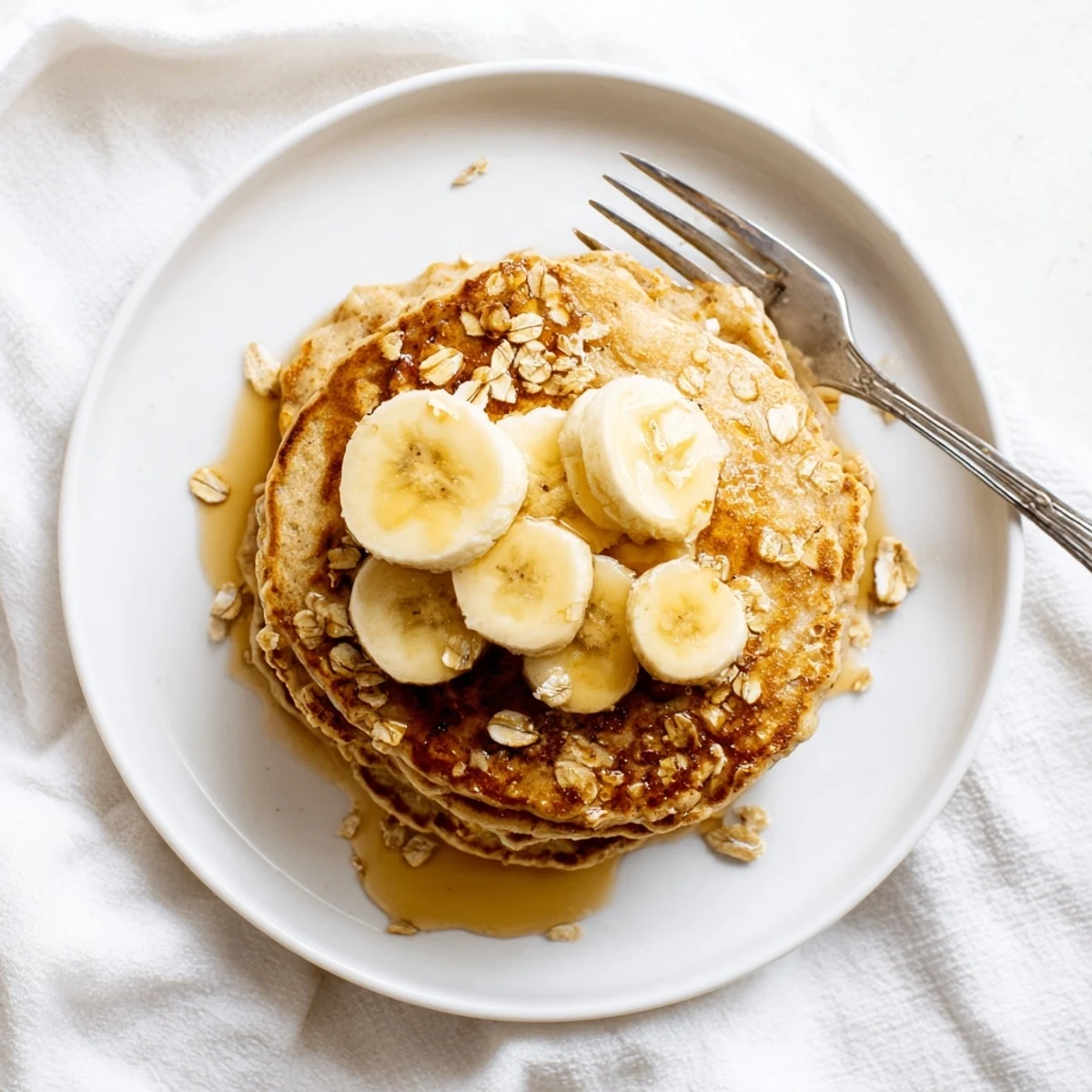 Golden-brown Banana Oat Pancakes simmering on a griddle with bubbling batter and a spatula ready to flip.  