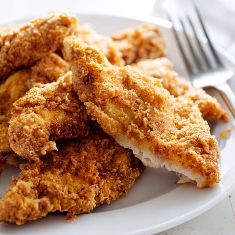 Golden-brown Crispy Fried Chicken Tenders rest on a wire rack, their seasoned crust glistening with flecks of paprika and cayenne.