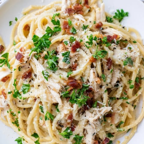 Steaming plate of creamy Chicken Carbonara with shredded chicken, crispy bacon, and al dente spaghetti twirled on a fork.  