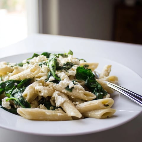 Creamy Feta Spinach Pasta features tender pasta coated in a rich, tangy sauce with vibrant wilted spinach and crumbled feta.