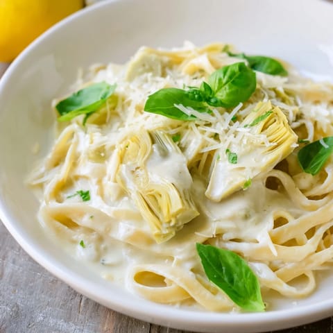 A beautiful bowl with creamy lemon artichoke pasta, topped with fresh herbs for a tasty meal.