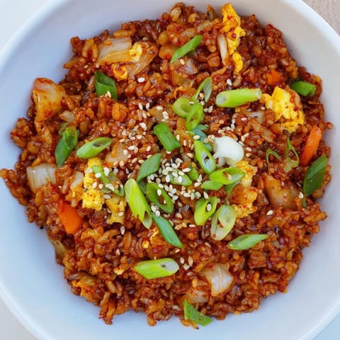 A close-up of golden, fluffy Spicy Kimchi Fried Rice with chunks of tangy kimchi and a softly scrambled egg mixed throughout.  