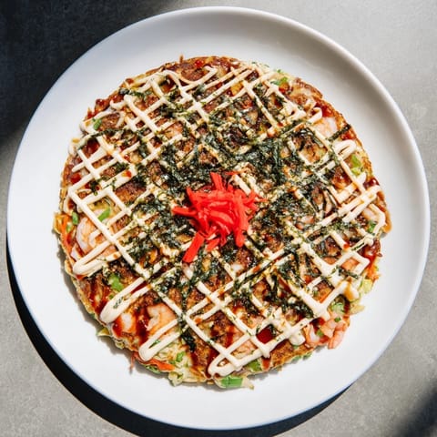 A close-up of fluffy Japanese Okonomiyaki Pancakes, drizzled with savory sauce and sprinkled with vibrant green aonori seaweed.