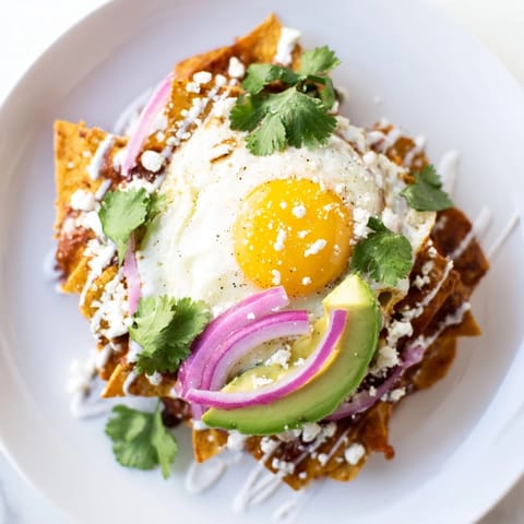 Golden chilaquiles covered in red salsa, garnished with cilantro, red onion, and a dollop of sour cream, served warm.  