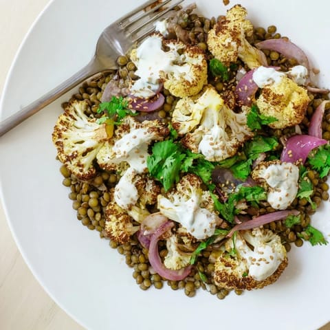 A top-down view of the Roasted Cauliflower With Lemon Lentil Cumin Tahini Yogurt platter, garnished with toasted sesame seeds and fresh cilantro.  