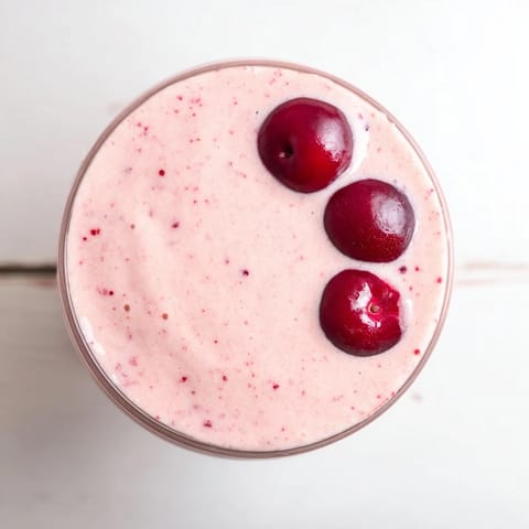 A tall glass of vibrant Cherry Almond Smoothie with creamy texture, garnished with sliced almonds and fresh cherries.