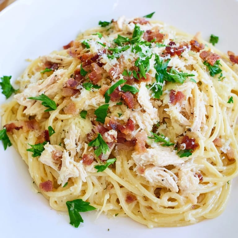 A close-up of Chicken Carbonara in a white bowl, garnished with parsley and extra grated Parmesan, ready to serve.  