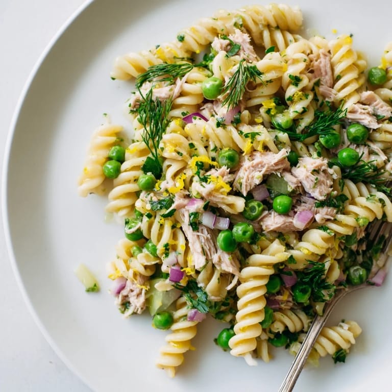 Picnic-ready Lemony Tuna Pasta Salad in a white serving bowl, garnished with dill and parsley, paired with a chilled glass of white wine.