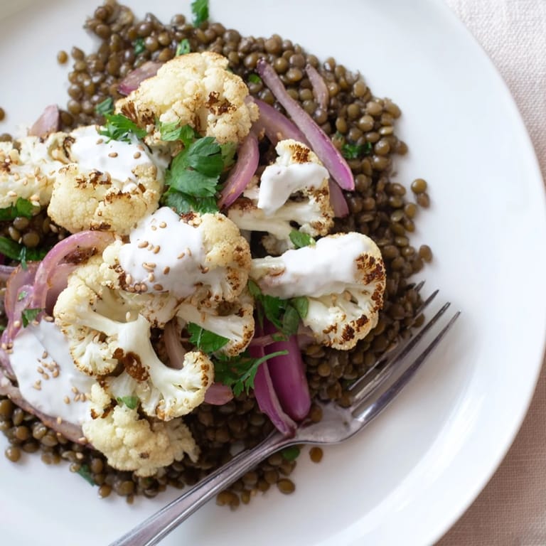 Spoonful of creamy cumin-tahini yogurt drizzled over caramelized cauliflower and zesty lemon lentils, served with lemon wedges on the side.