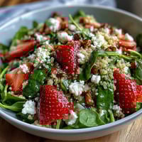 A colorful bowl of strawberry feta quinoa salad with juicy berries, creamy cheese, and fresh greens drizzled with balsamic dressing.