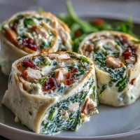 Turkey, cheese, and spinach tortilla pinwheels with creamy spread, sliced into colorful spirals perfect for lunchboxes or party trays.